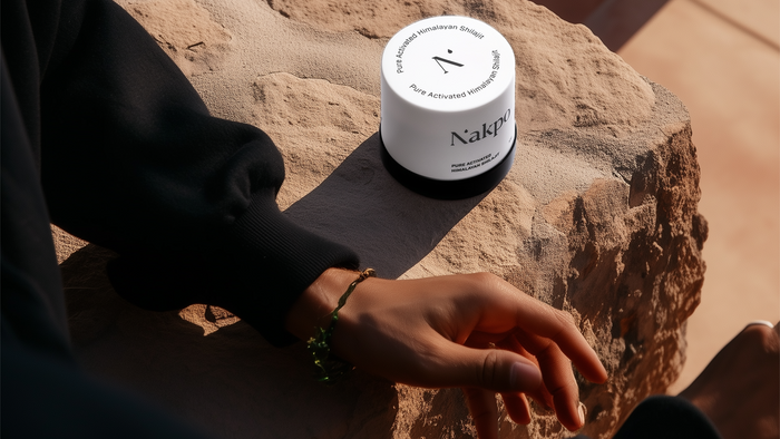 Jar of Nakpo Pure Activated Himalayan Shilajit resting on a natural stone surface, with a relaxed hand nearby, showcasing premium wellness branding in a serene outdoor setting.