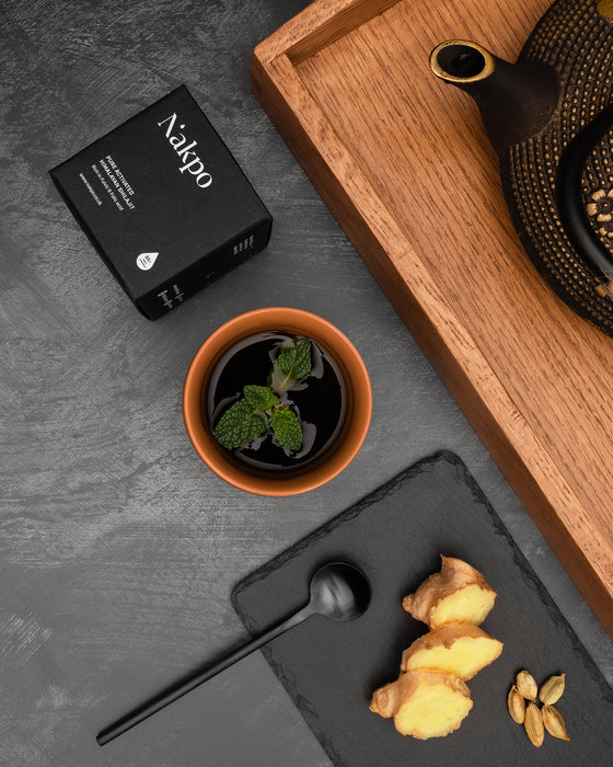 Nakpo Shilajit box beside a traditional tea set, mint leaves, and fresh ginger slices, offering Himalayan Shilajit rich in B12 and fulvic acid for natural vitality.